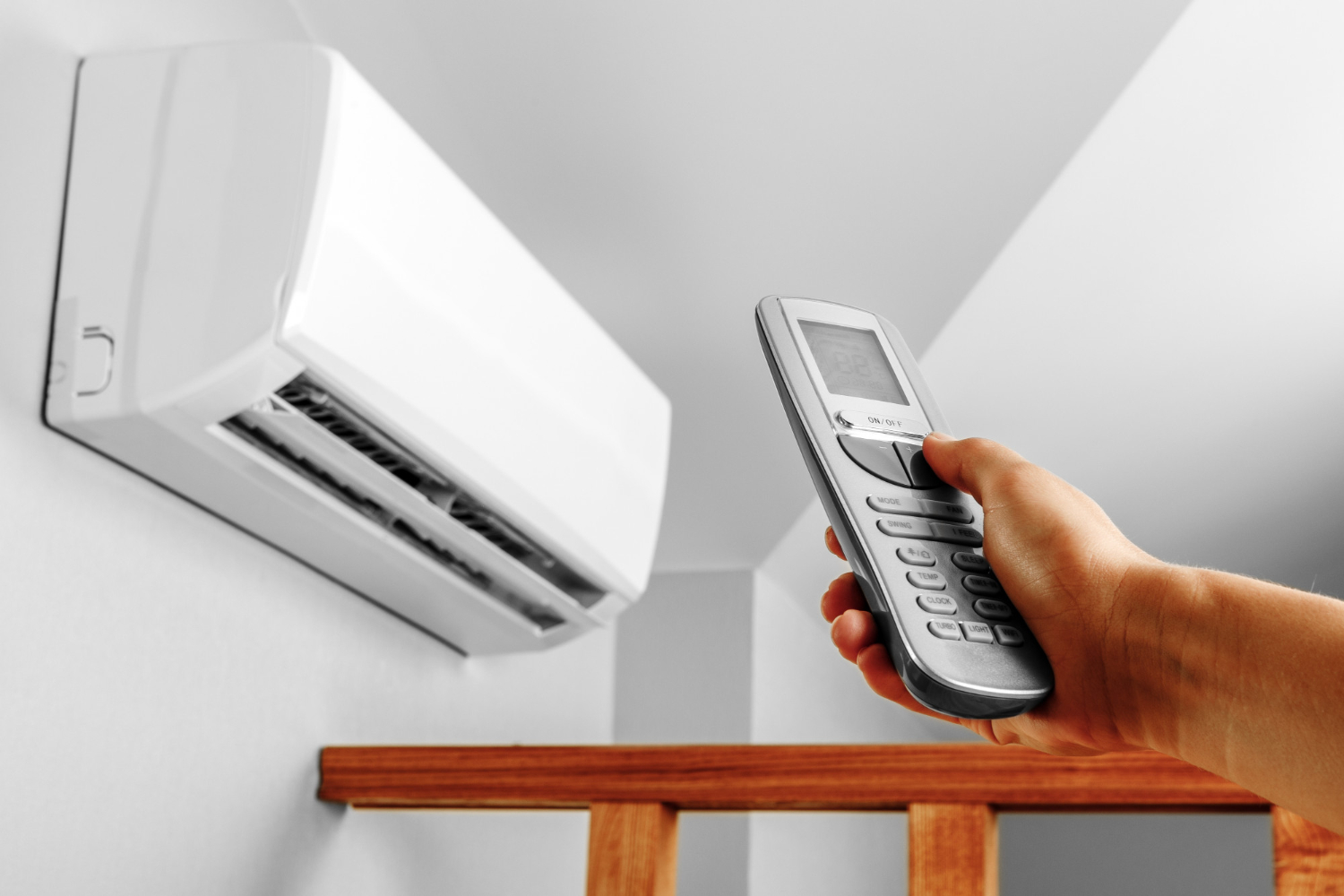 HVAC Blog 4 Hand holding remote control aimed at a wall-mounted air conditioning unit, illustrating HVAC system operation in a home environment.